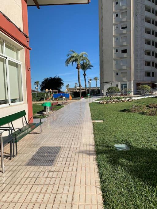 a brick walkway with benches and palm trees in a park at Apartamento Alicante San Juan playa 1ª línea in Benimagrell