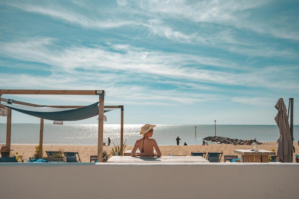 uma mulher sentada na praia a olhar para o oceano em Hôtel Le Rivage vue sur mer - Châtelaillon-plage em Châtelaillon-Plage