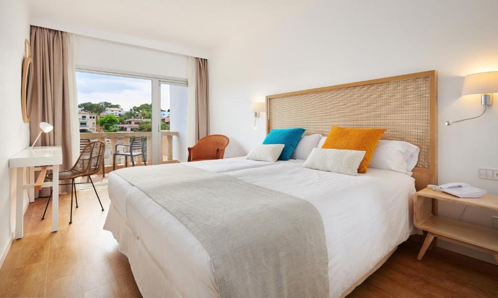 a bedroom with a large white bed and a balcony at Hotel Apartamentos Cala Santanyi in Cala Santanyi