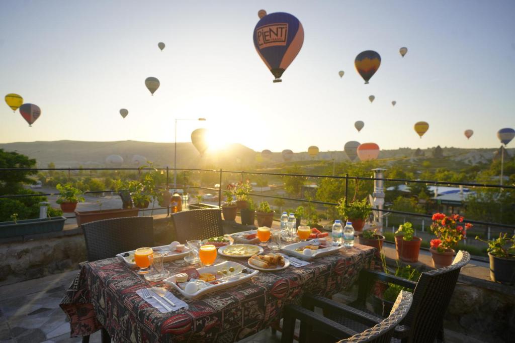 une table avec de la nourriture et des ballons à air chaud dans le ciel dans l'établissement Lucky Luke Stone House, à Gorëme