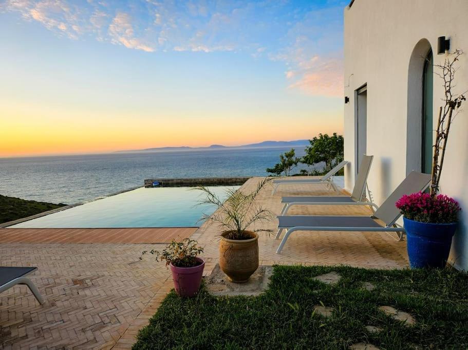 Très belle villa avec piscine et vue incroyable sur mediterannée (DAR NAIM) في طنجة: مجموعة من المقاعد للجلوس على جانب المنزل
