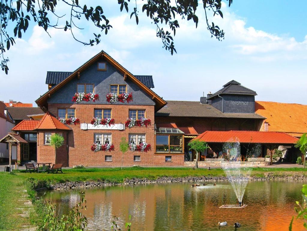 un bâtiment avec une fontaine en face d'un étang dans l'établissement Der Teichhof, à Grandenborn