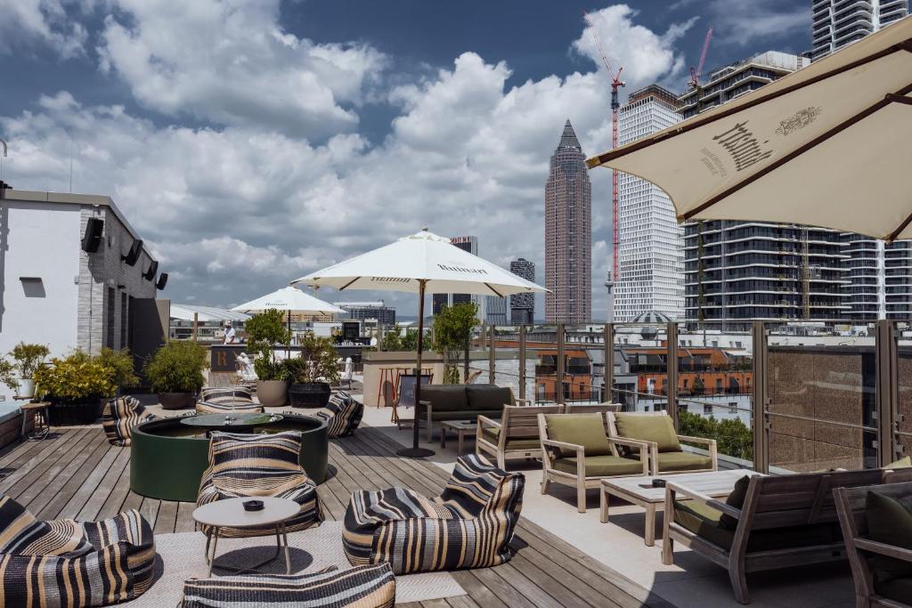 a rooftop deck with chairs and tables and a city skyline at Gekko House Frankfurt, a Tribute Portfolio Hotel in Frankfurt/Main
