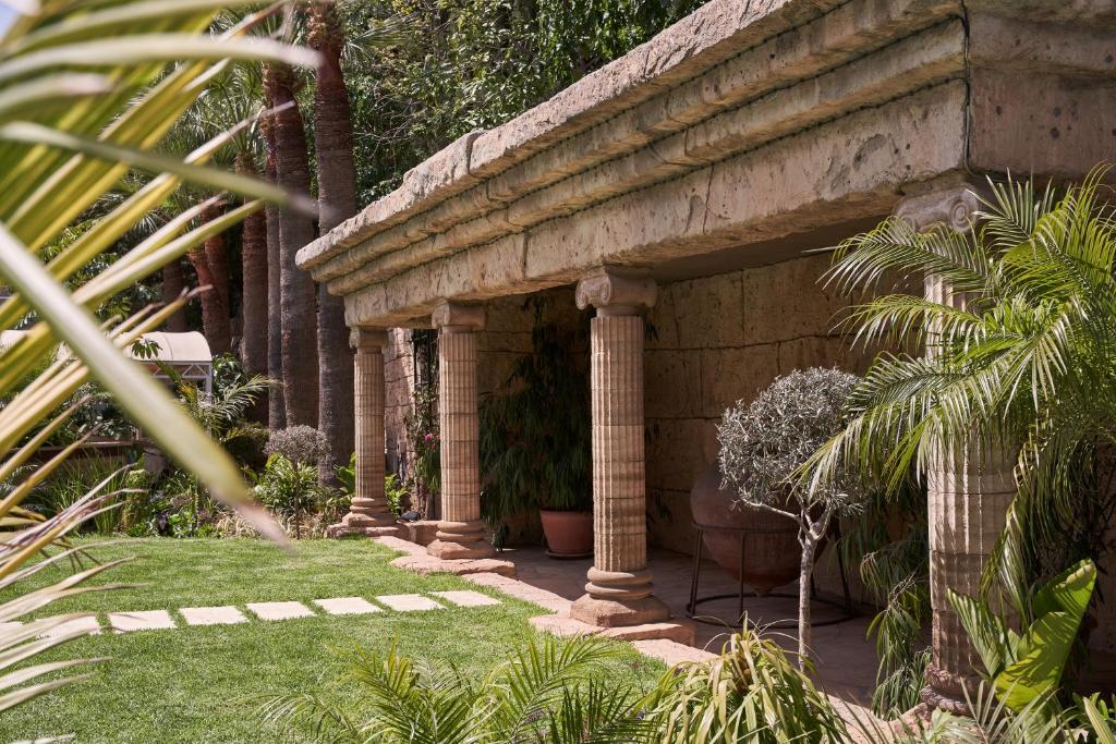 a stone building with columns and plants in a garden at Atlantica Bay - Adults Only in Limassol