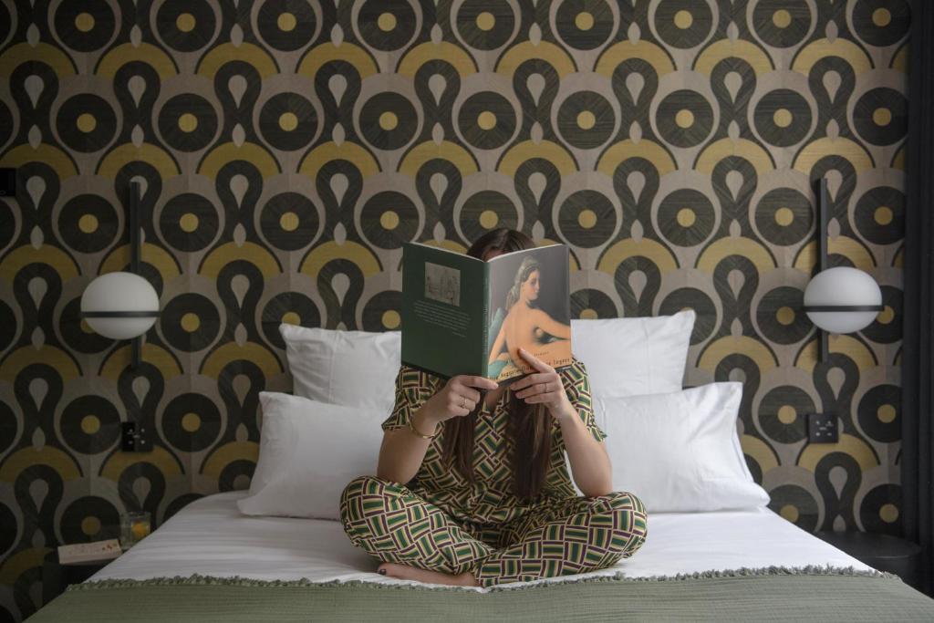 una persona sentada en una cama leyendo un libro en MiHotel Sala en Lyon