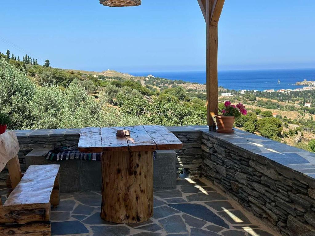 una mesa de madera y bancos en una pared de piedra con el océano en Richie's Sea View Romantic Residences, en Ándros
