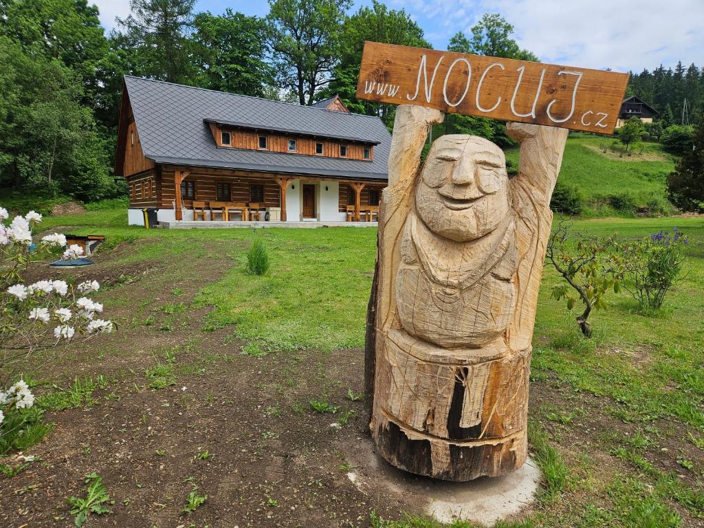 una estatua de madera con un cartel delante de una casa en Nocuj, en Teplice nad Metují