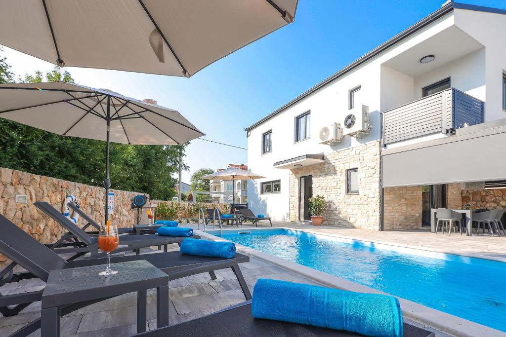 a villa with a swimming pool with a table and an umbrella at Villa Kaoru brand new Villa with a heated swimming pool in Malinska
