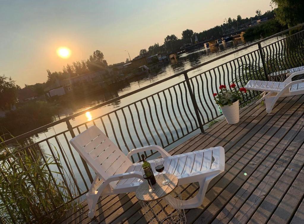 two white benches sitting on a deck overlooking a body of water at Ostoja Nad Rzeką in Łeba