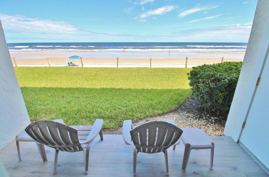 eine Terrasse mit 2 Stühlen, einem Tisch und einem Strand in der Unterkunft Colony Beach Club 128 in New Smyrna Beach