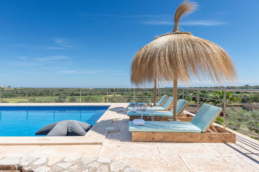 a pool with two lounge chairs and a straw umbrella at Sa Plana Nova in Portocolom
