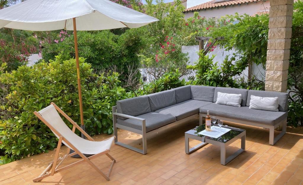 een patio met een bank, een parasol en een tafel bij Lady Blue, villa à 15 mn plage à pied, parking, wifi, jardin in La Grande-Motte