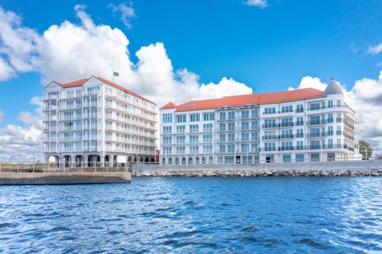 two large white buildings with red roofs on the water at Marina Royale Darłowo - Apartamenty Ultra Mar nad morzem in Darlowko