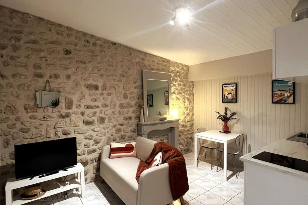 シャンプニエにあるGîte aux portes d'Angoulêmeの石壁のリビングルーム(ソファ、テレビ付)