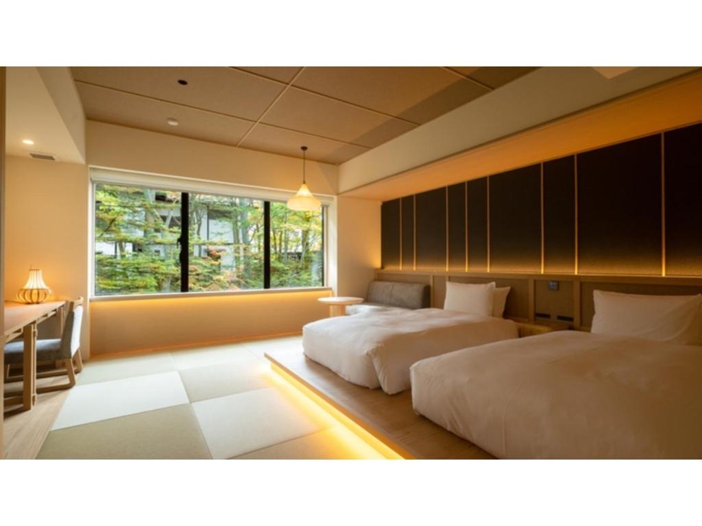 een slaapkamer met 2 bedden, een bureau en een raam bij URAKUSATSU TOU - Vacation STAY 75063v in Kusatsu