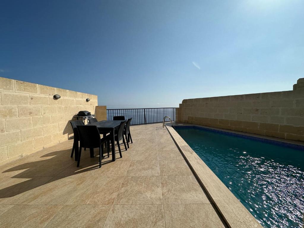 patio ze stołem i krzesłami przy basenie w obiekcie Hili Complex w mieście Żebbuġ