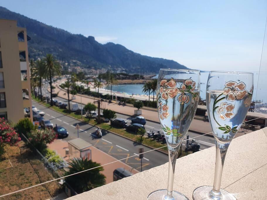 deux verres à vin assis sur un livre avec vue sur une ville dans l'établissement Le Garavan, Superbe studio vue mer et vieux Menton, à Menton