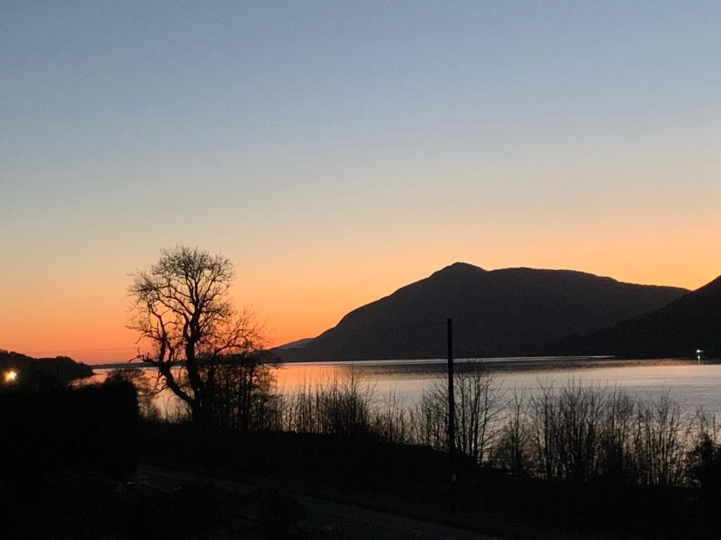 un coucher de soleil sur un lac avec des montagnes en arrière-plan dans l'établissement Ormasaig, Self Catering, One Mile to Town & close to Ben Nevis, à Fort William