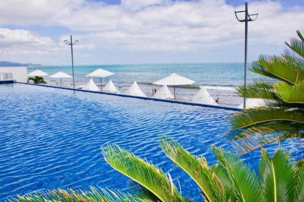 a swimming pool next to the ocean with white umbrellas at Grand Diamond Beach, Dep 2 dormitorios in Tonsupa