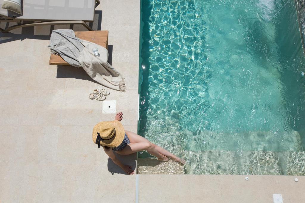 Una mujer con sombrero sentada junto a una piscina. en Muses of art Villas, en Afantou
