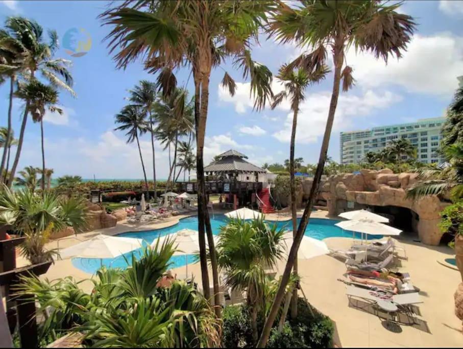 una piscina en el complejo con palmeras y sillas en Modern Miami Beach Condo with Beach Service & Pool, en Miami Beach