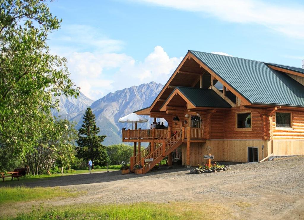a log cabin with a deck and mountains in the background at Majestic Valley Wilderness Lodge in Sutton