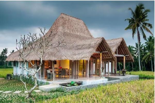 uma casa com telhado de palha e um campo em Bennu House em Ubud