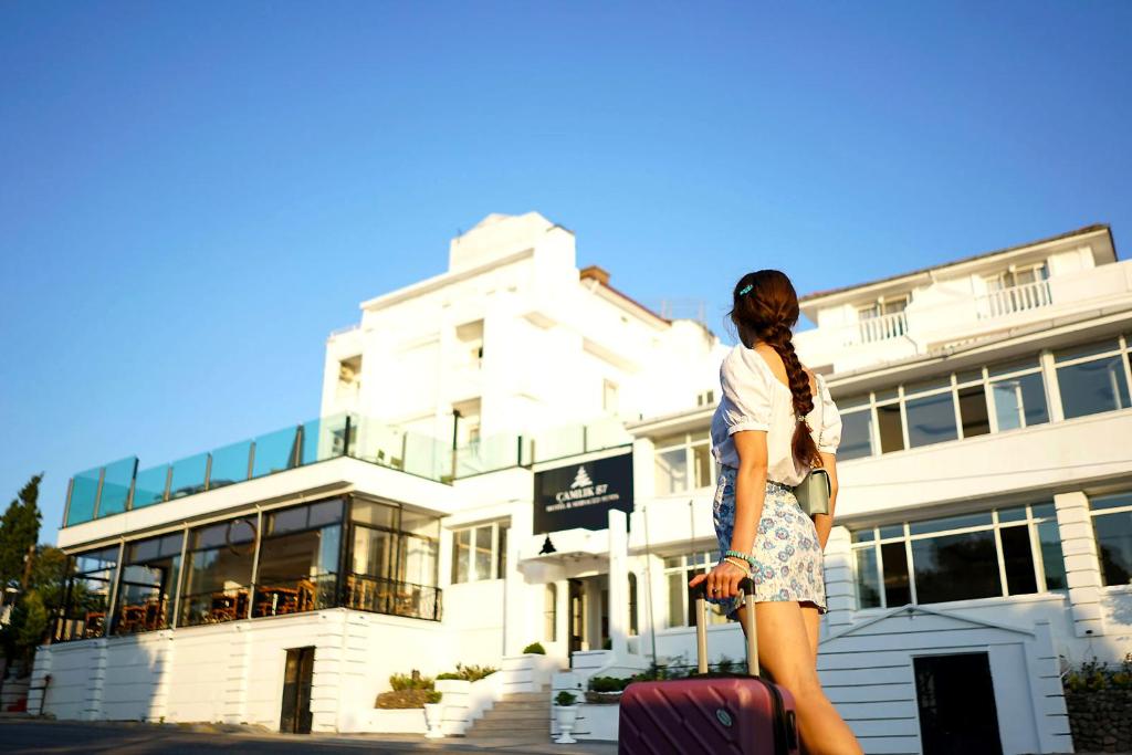 a woman standing in front of a building with luggage at Çamlık 87 Hotel Ayvalık in Ayvalık