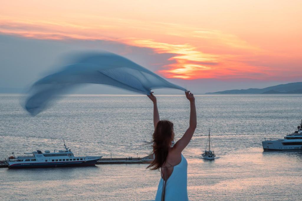 a woman with her arms in the air near the water with boats at Petasos Chic Hotel in Mýkonos City