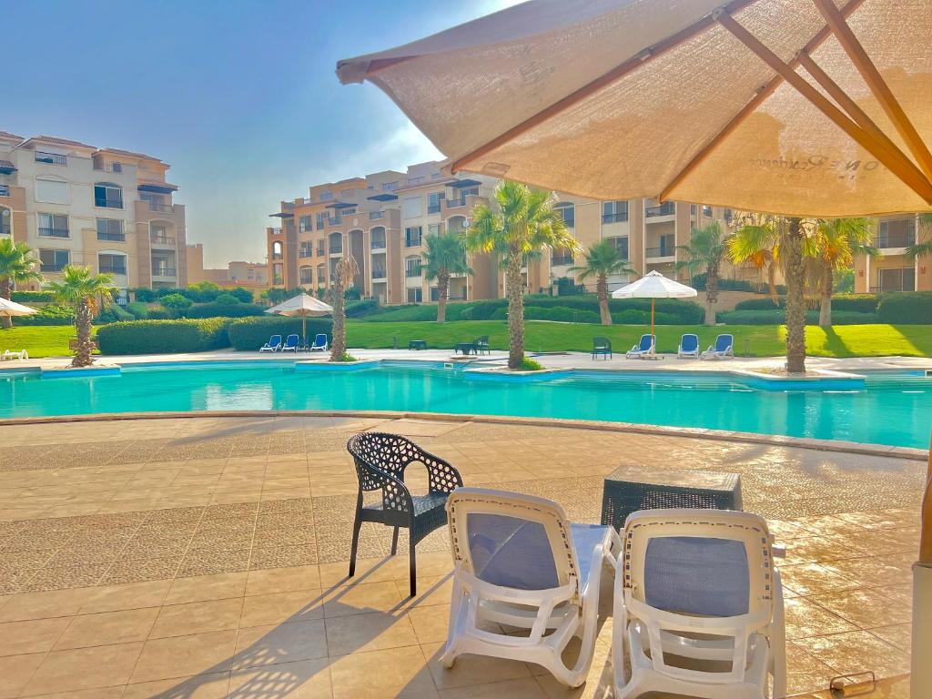 due sedie e un ombrellone accanto alla piscina di Ultra Luxury 3BR with Pools ,Sports ,Dining in Gated compound, Close to all sites a Il Cairo