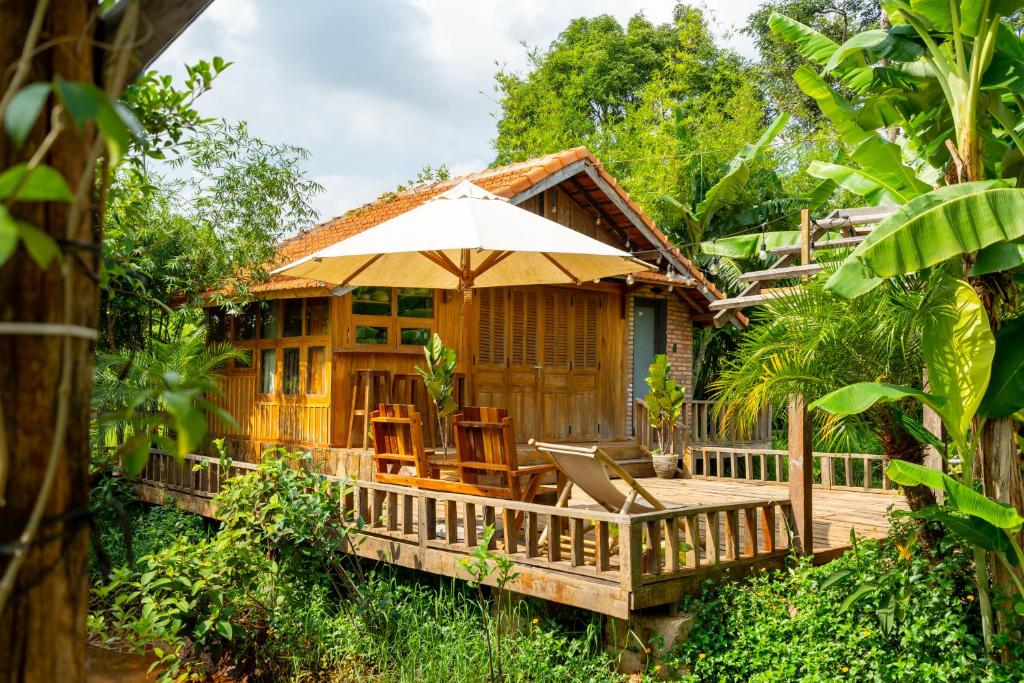 a house with a deck with chairs and an umbrella at Mộc An Nhiên Farmstay in Pleiku