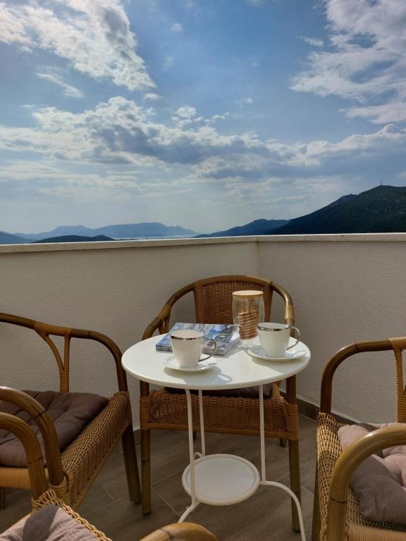 a table with two cups and chairs on a balcony at Apartmani Sunset in Neum