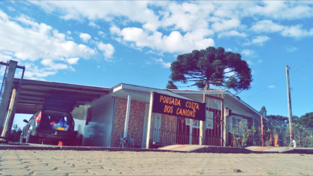 a sign in front of a building with a tree at Pousada Costa dos Canions in Cambará
