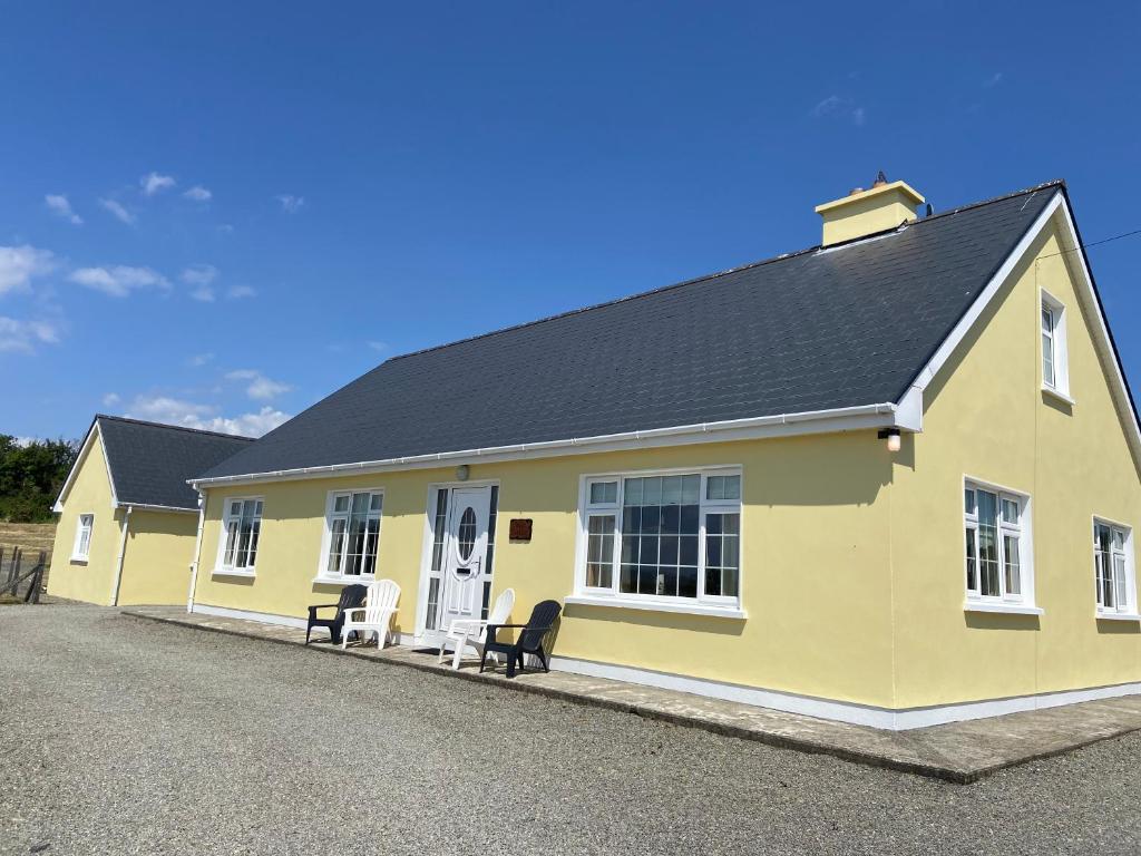 una casa amarilla con dos sillas delante en Tilly's Cottage, en Durrus