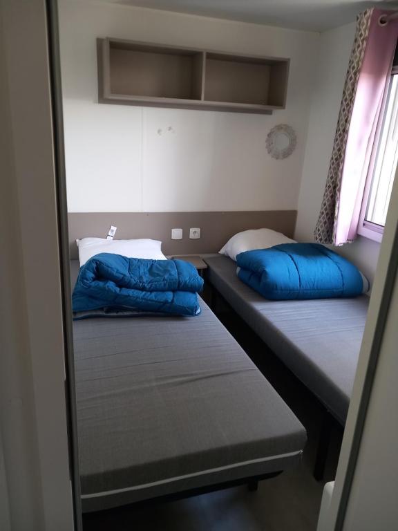 two beds in a small room with blue pillows at Mobil-home Les Dunes de Contis in Saint-Julien-en-Born