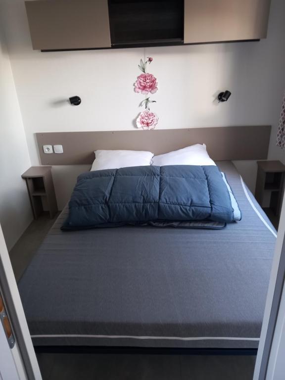 a bed with a blue comforter and two pillows at Mobil-home Les Dunes de Contis in Saint-Julien-en-Born