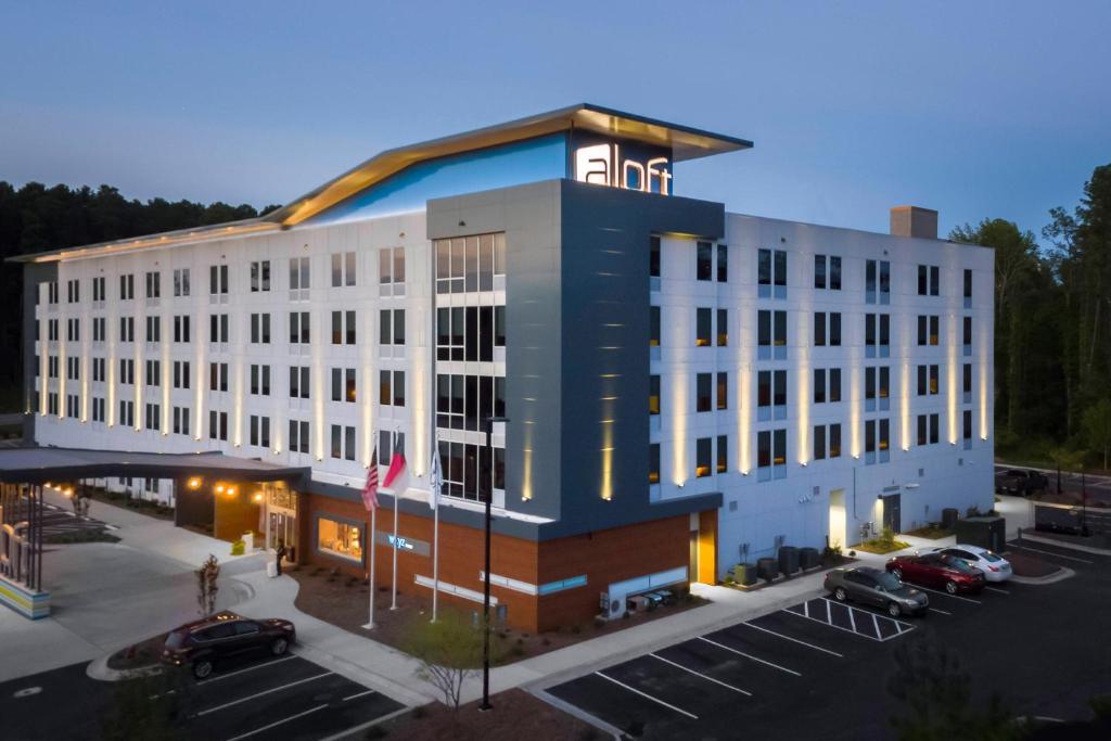 a large white building with cars parked in a parking lot at Aloft Raleigh Durham Airport Brier Creek in Raleigh