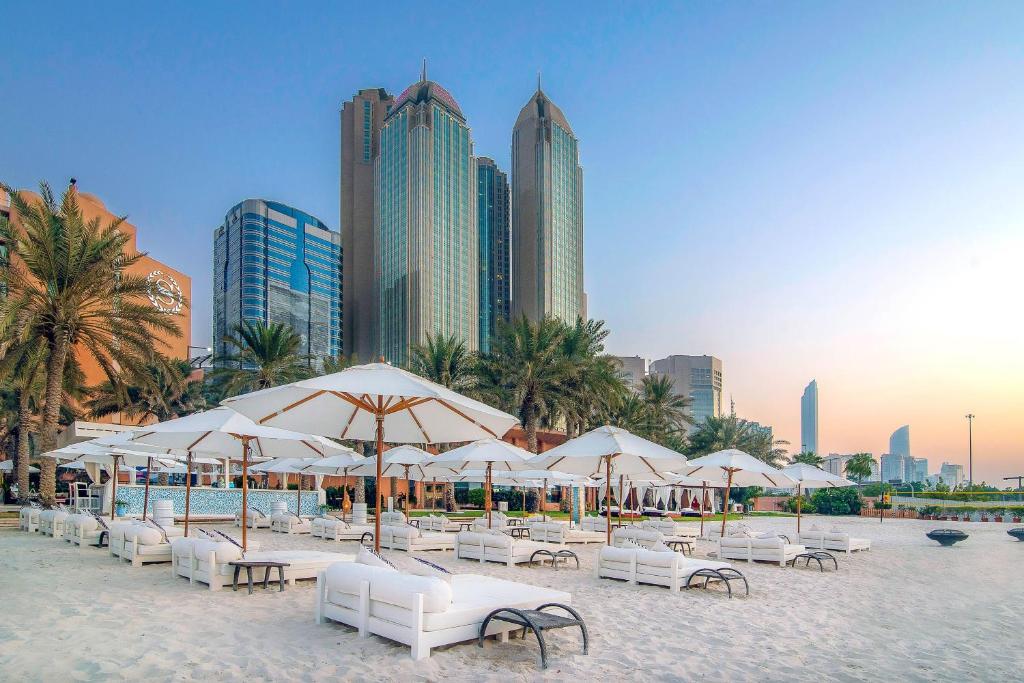 een strand met witte stoelen, parasols en gebouwen bij Sheraton Abu Dhabi Hotel & Resort in Abu Dhabi