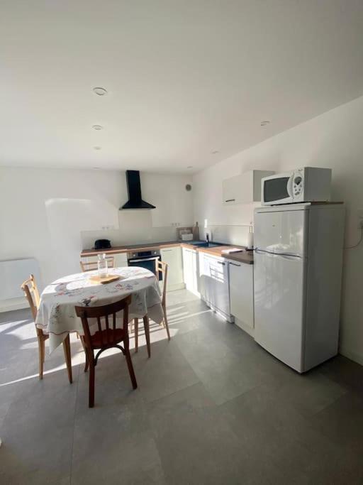 a kitchen with a table and a white refrigerator at REZ DE JARDIN AU COEUR DES PYRENEES in Agos-Vidalos