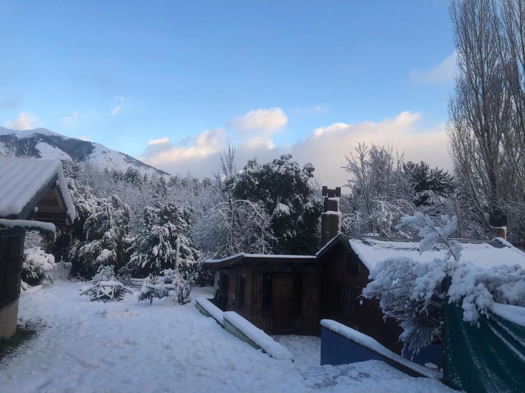 un patio cubierto de nieve con una casa con chimenea en Cuatro Cerros Hostel en San Carlos de Bariloche