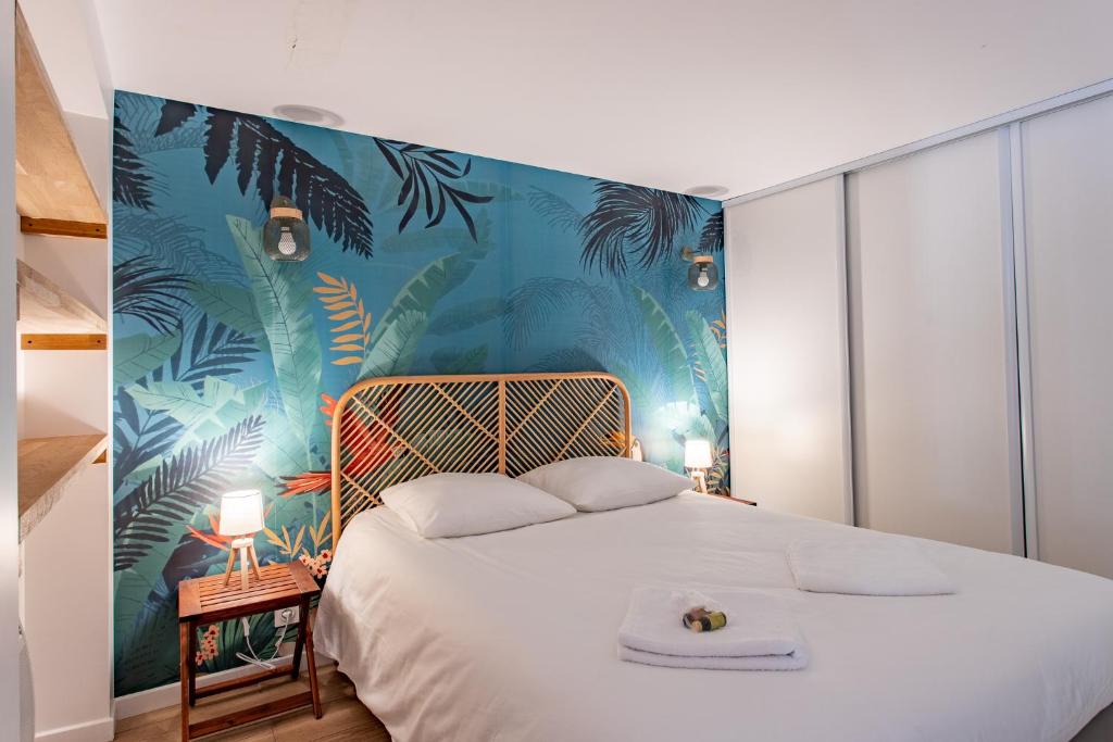 a bedroom with a white bed with a tropical wallpaper at Villa des Sables in Lège-Cap-Ferret