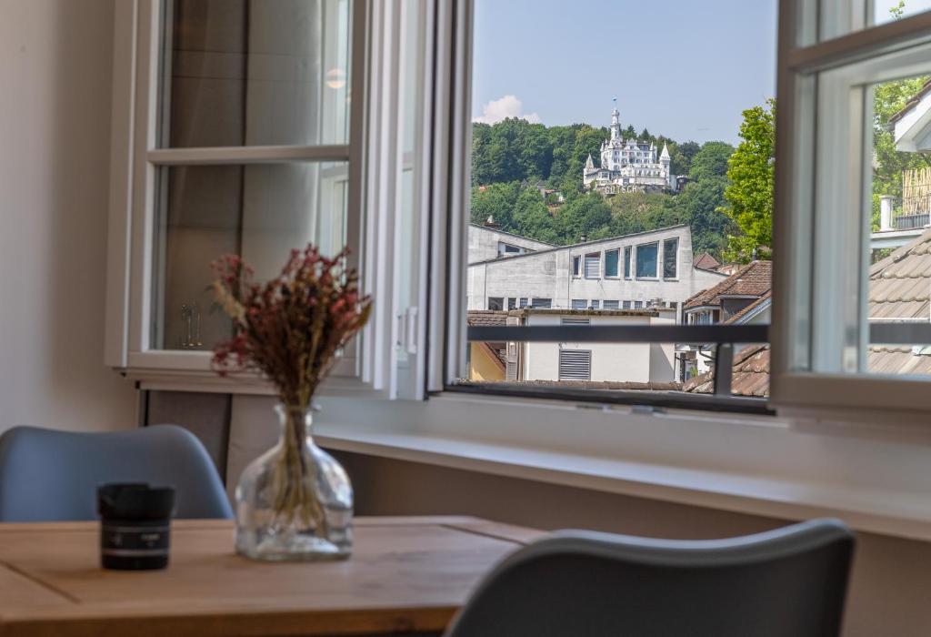 eine Vase mit Blumen auf einem Tisch vor einem Fenster in der Unterkunft KoBi Apartments Falkenplatz in Luzern