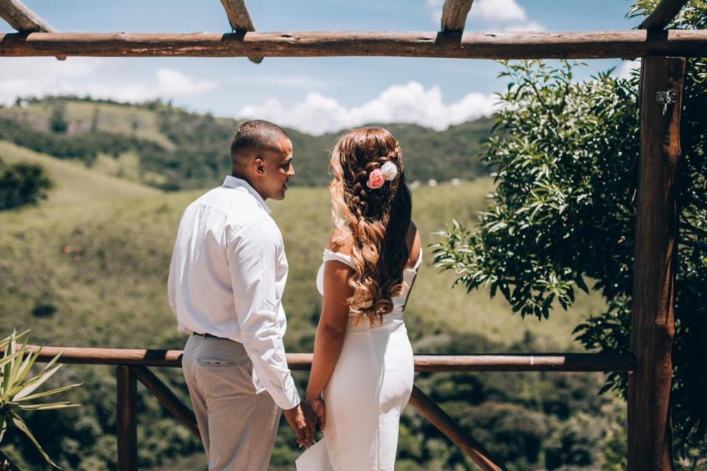 Una novia y un novio parados junto a una valla en Canto do Vento Hospedaria, en Santo Antônio do Pinhal