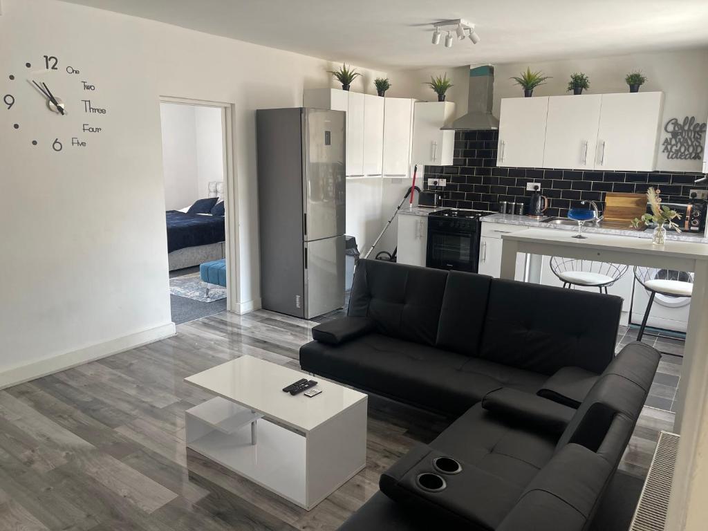 a living room with a black couch and a kitchen at Spacious 3 bed flat near Watford Junction in Watford