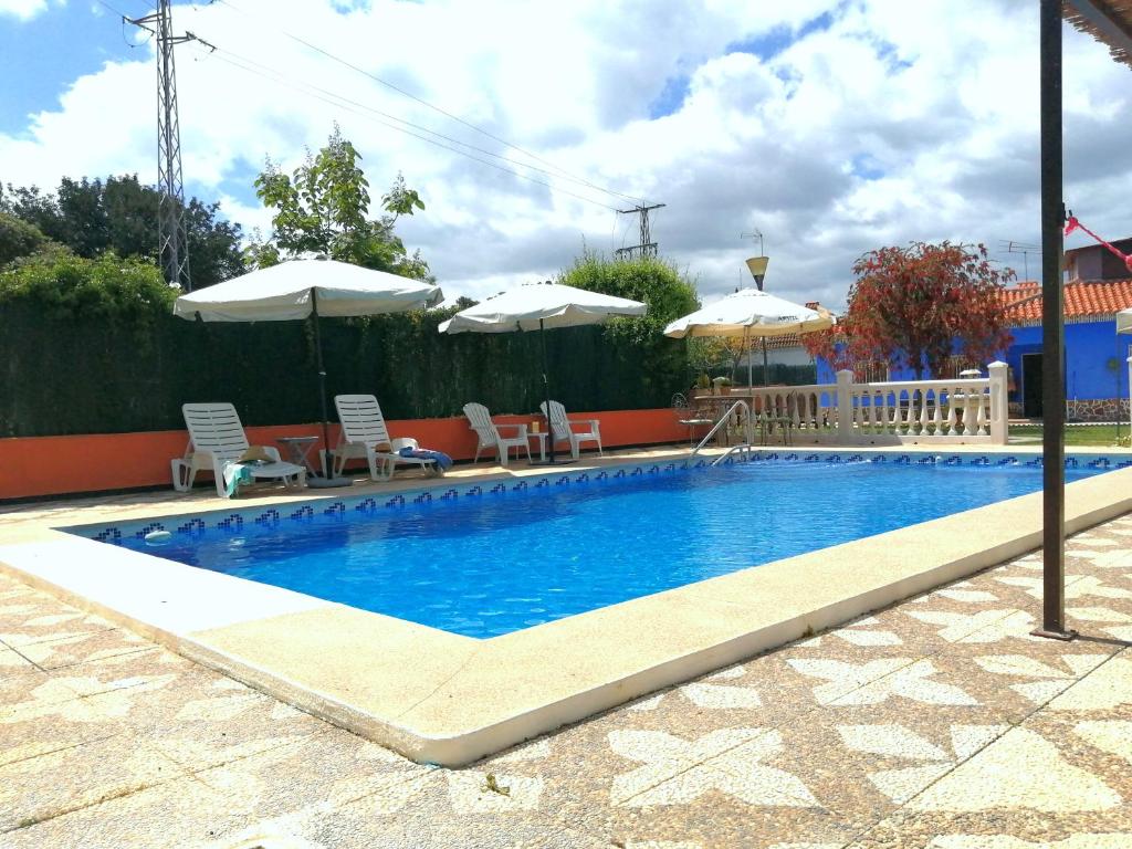 una piscina con sillas y sombrillas junto a ella en La Morada del Yayo 15 minutos de Sevilla, en Las Pajanosas