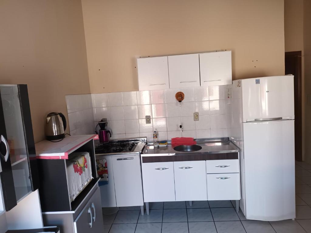 uma cozinha com armários brancos e um frigorífico branco em Kitnet em Tramandaí