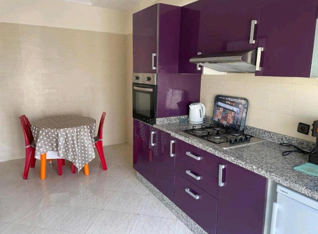 a kitchen with purple cabinets and a table with chairs at Vue sur mer in Sidi Rahal