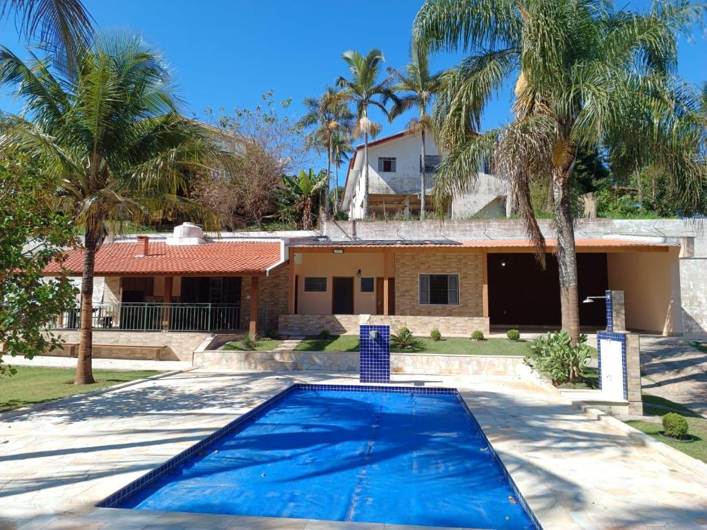 a swimming pool in front of a house with palm trees at Chácara Rancho Fundo in Águas de Lindoia