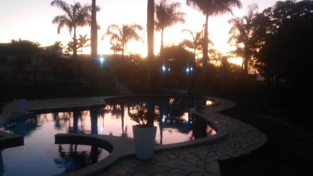 una piscina con palmeras y una puesta de sol en Pousada Serra Azul en Tiradentes
