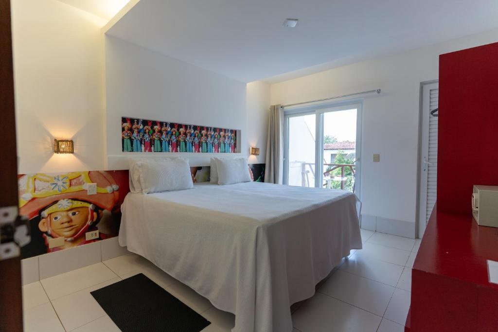 a bedroom with a white bed with a painting on the wall at Galeria e Suites Canto do Sol in Barra Grande